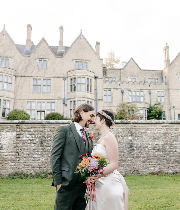 Bride and groom walking towards Minstead Lodge with autumn leaves in the distance